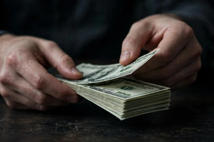 يد تعد أوراقًا نقدية من فئة 100 دولار أمريكي — سعر الدولار في العقود الآجلة